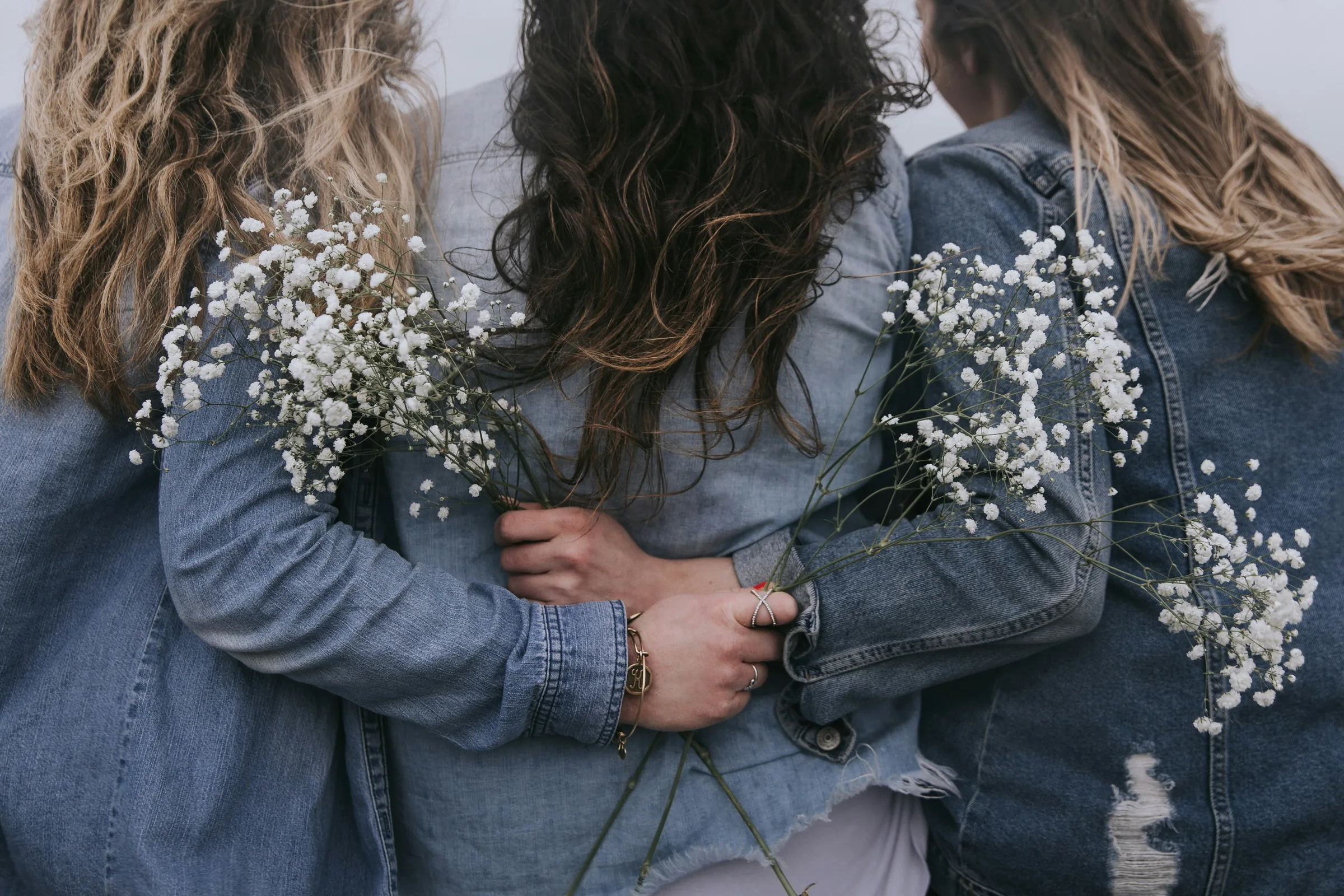 Three girls with wildflowers in denim jackets, arm in arm